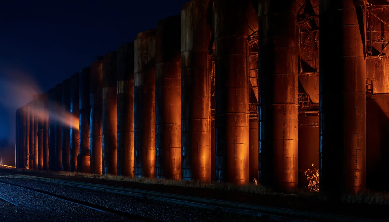 A row of rusted coke-oven doors receding into the dark, washed in deep red light.