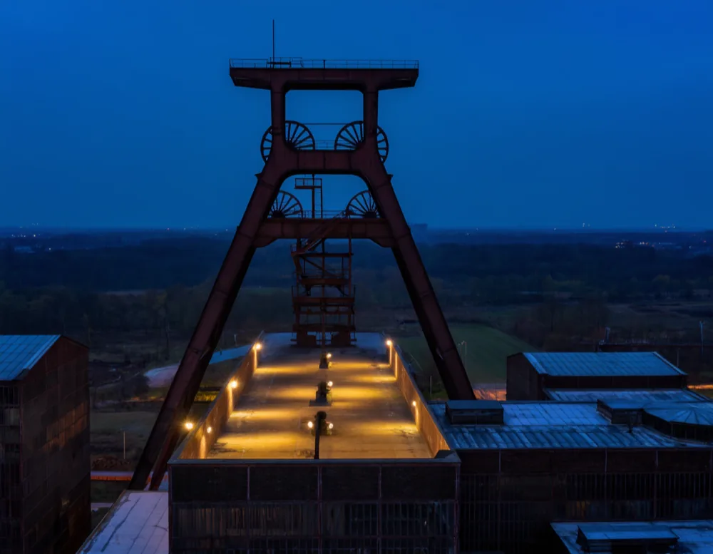 The steel headframe of the mine at dusk, sheave wheels above a lit platform deck.