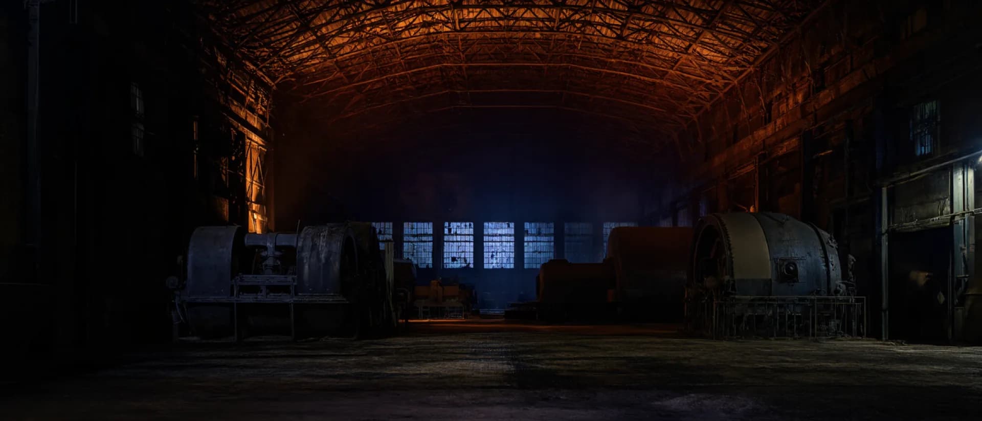 The winding-engine hall at night, riveted steel roof trusses lit deep red above the machinery.